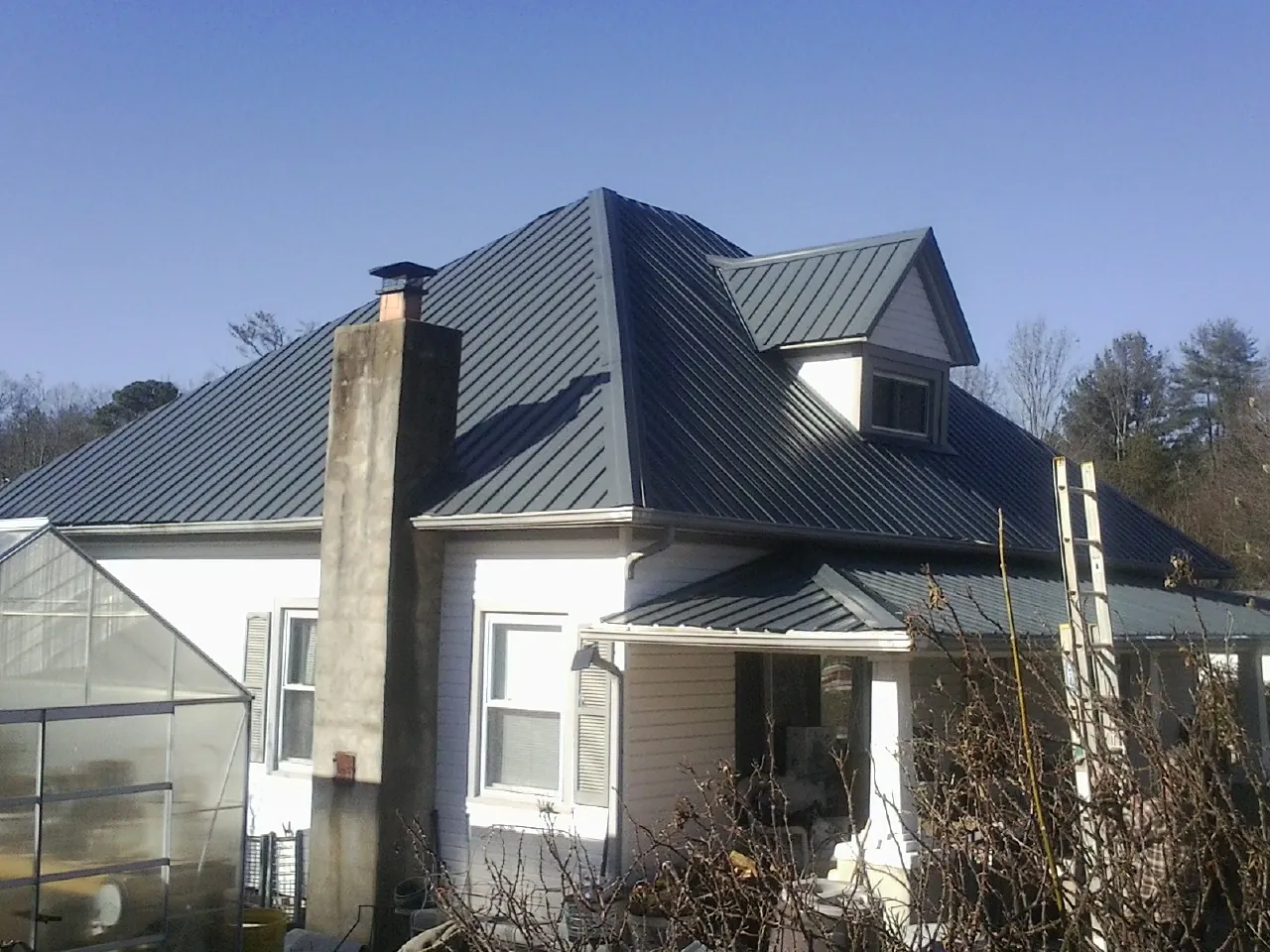 Dark blue standing seam metal roof on a white farmhouse with dormer — Slate & Tile Roof Repair by Roofing Brothers in Holmes