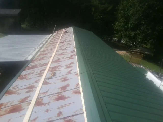 Old rusted panels beside newly installed green metal roofing — Wind Damage Roof Repair by Roofing Brothers in Holmes