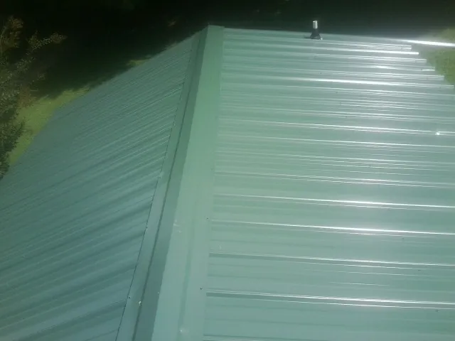 New green metal panels meeting at the ridge of a roof — Flat Roof Repair work by our crew in Holmes