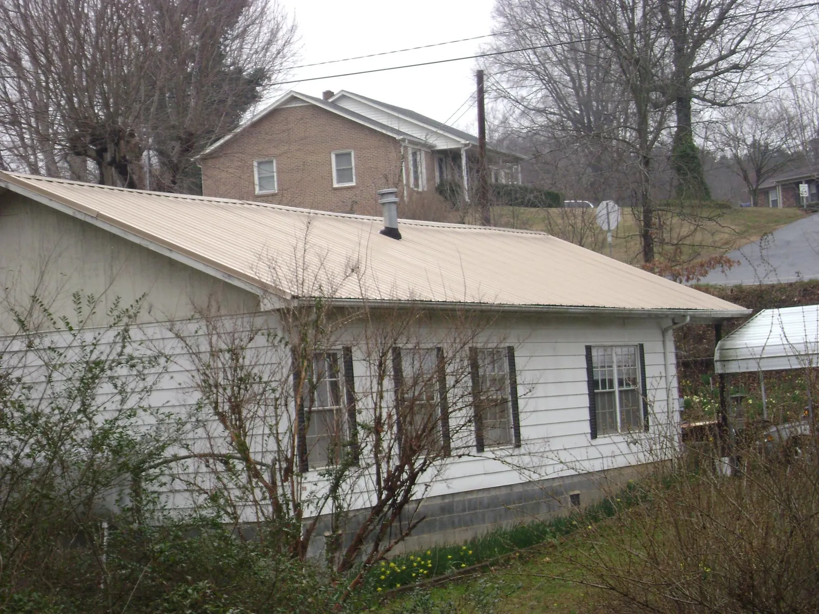 Tan metal roof on a white sided house set into a hillside — Commercial Roofing by Roofing Brothers in Holmes