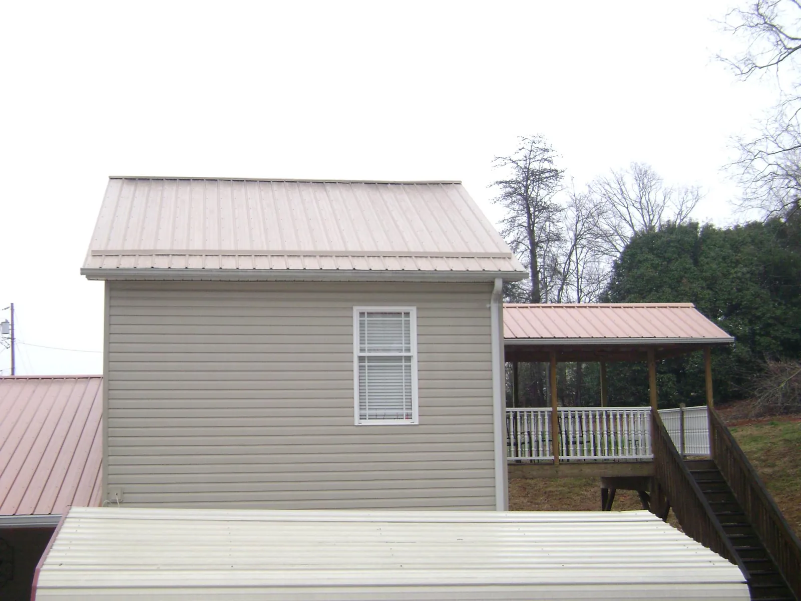 Tan metal roofs on a two story addition and attached porch, from a Roof Replacement job in Holmes