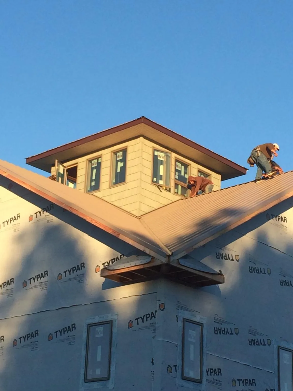 Roofers working around a rooftop cupola on a new metal roof at sunset — Roof Waterproofing in Holmes by Roofing Brothers